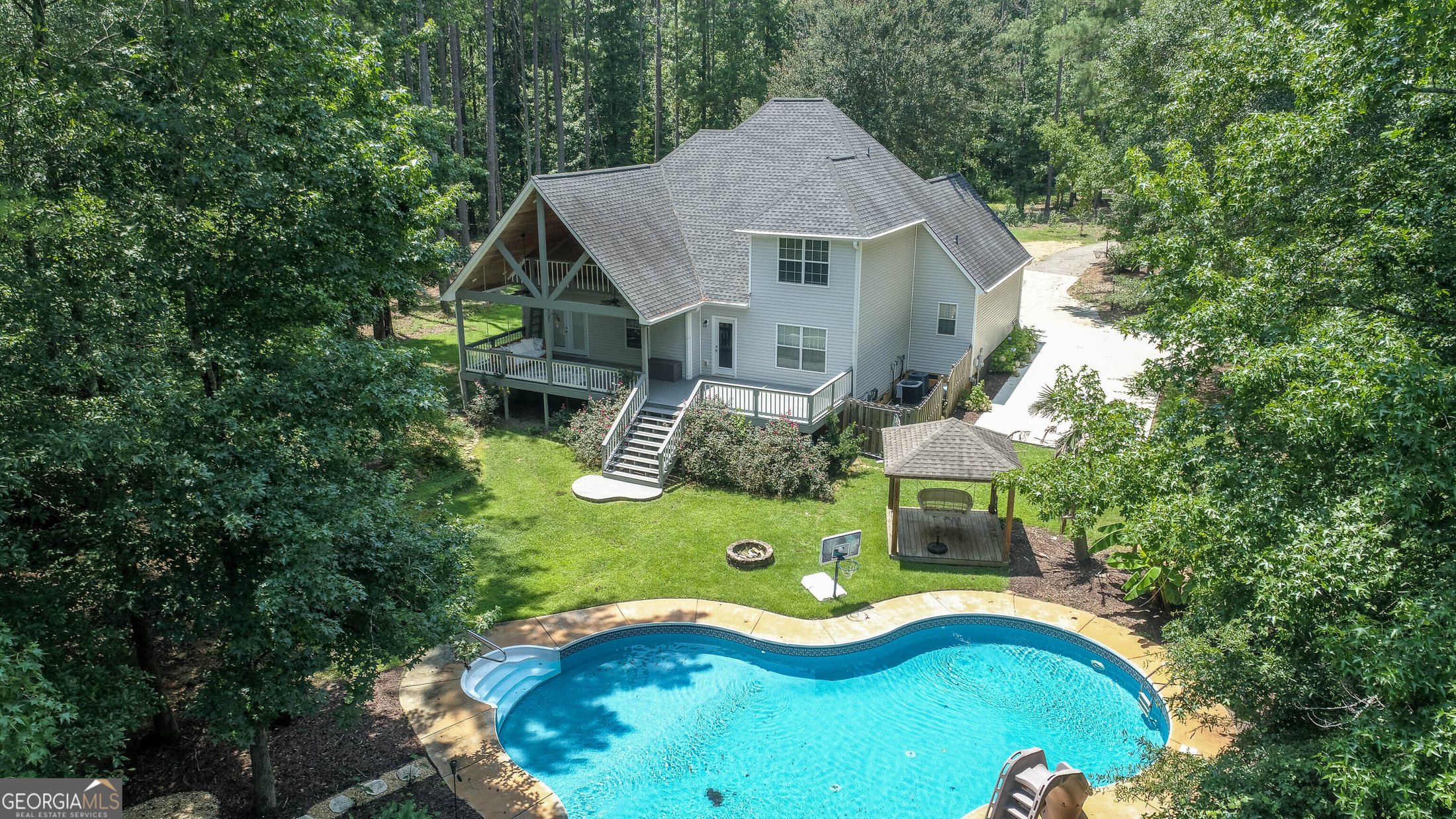 Aerial view of a private home, pool, and wooded lot